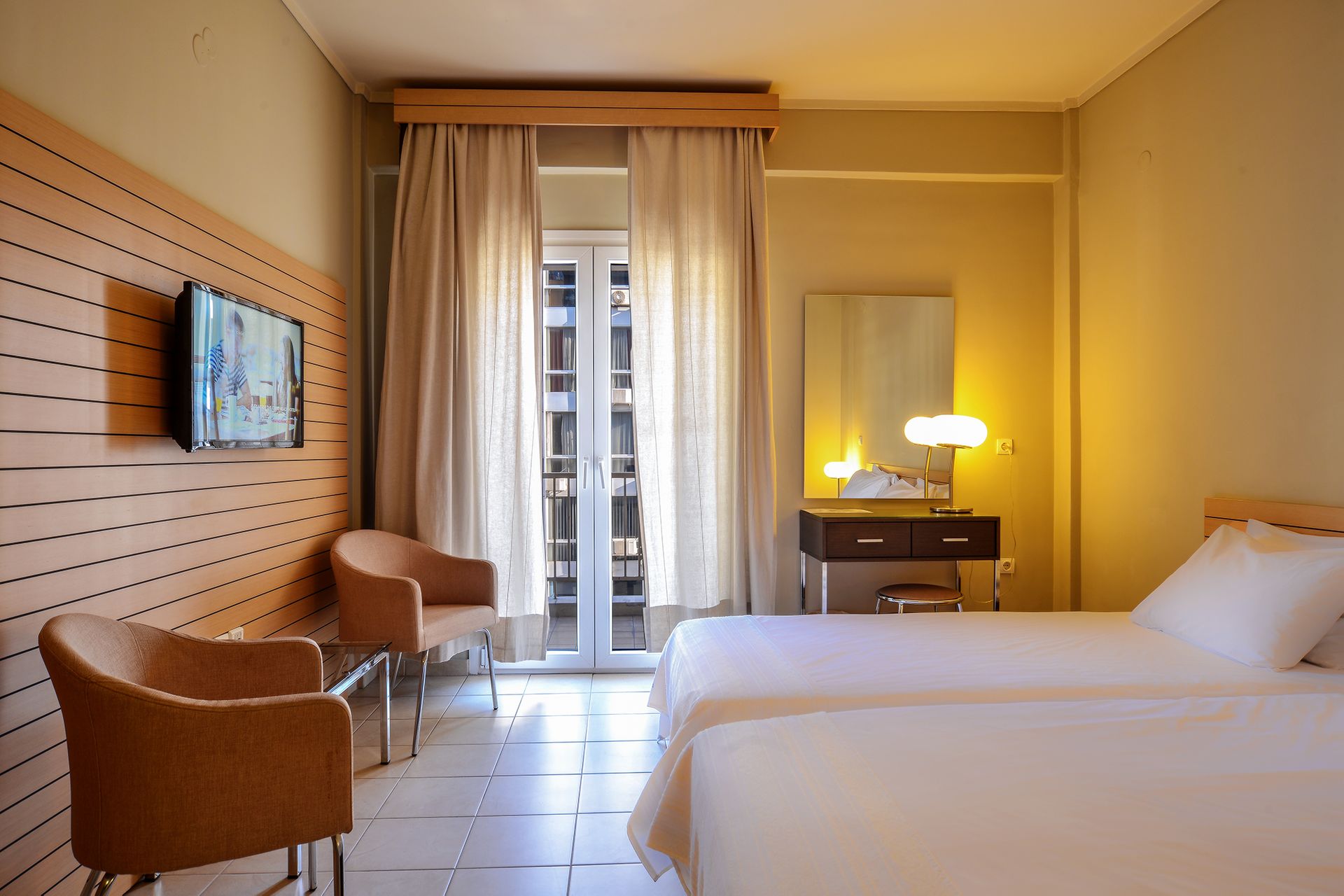 The bright light city view rooms at Astoria Hotel Thessaloniki offer a serene yet vibrant retreat, combining modern elegance with natural charm. Large windows bathe the space in abundant natural light, showcasing stunning views of Thessaloniki's live